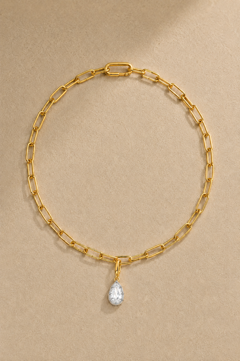 Gold paperclip chain necklace with mixed-metal Vittoria crystal charm on beige studio background
