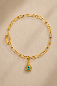 Gold paperclip bracelet with turquoise triangle evil eye charm on beige background