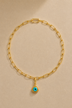 Gold paperclip chain necklace with turquoise triangle evil eye charm on beige background