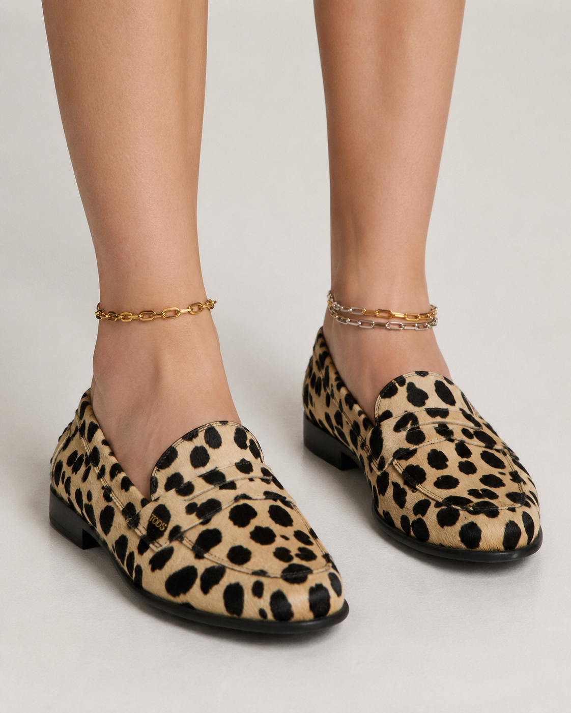 Gold and silver anklets by Galleria Armadoro styled asymmetrically with leopard-print loafers for a polished office jewellery look.