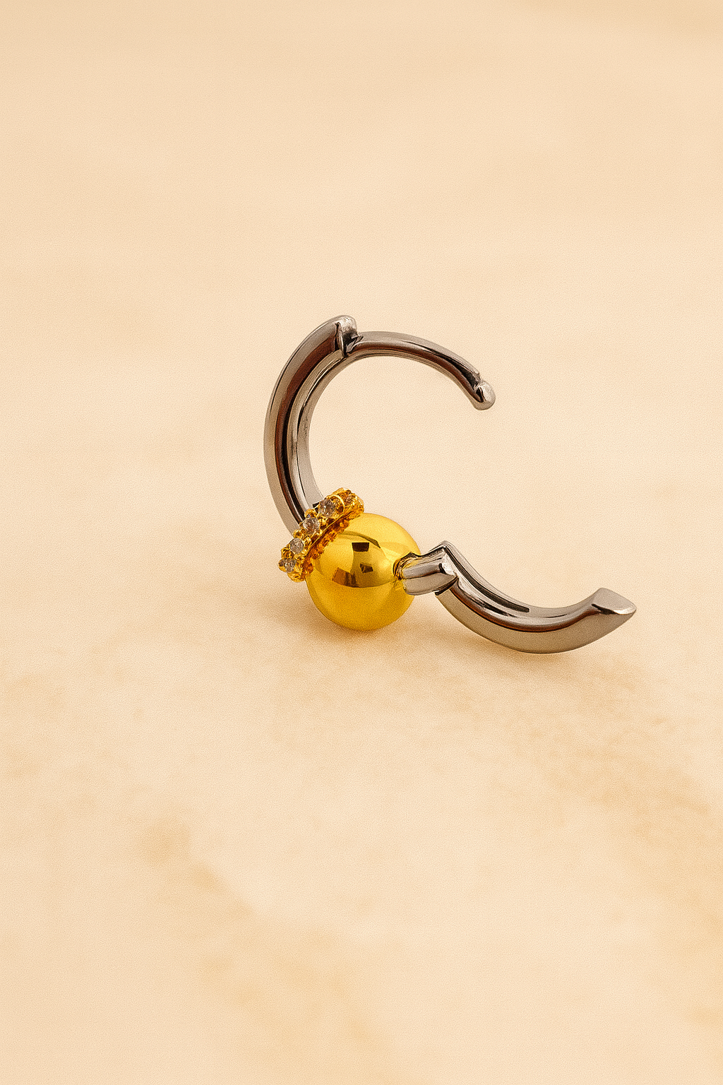 Pair of Kora two-tone bead huggie earrings on matte beige surface showing full CZ halo detail