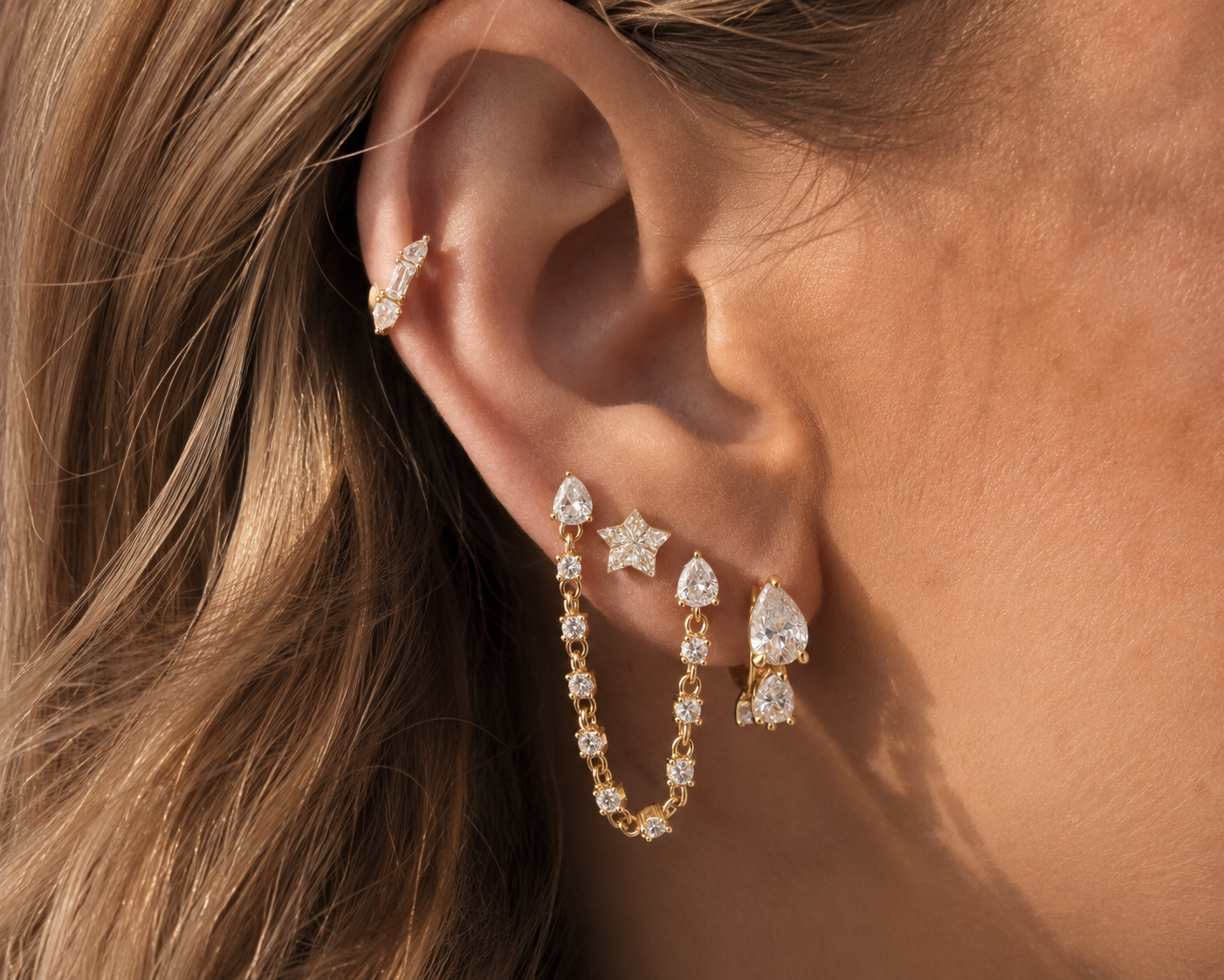 Gold ear stack styled by Galleria Armadoro with linked chain earrings, a star stud, teardrop earrings and a delicate upper-ear detail.