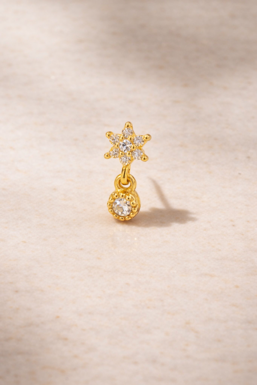 Romy Stud 24ct gold plated single stud earring with star and drop white CZ on matte beige marble background