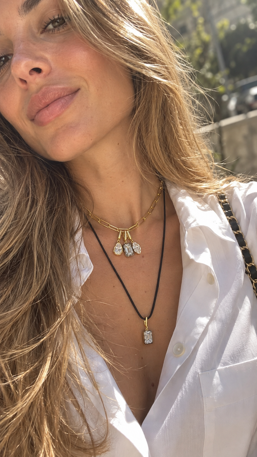 Layered Galleria Armadoro necklaces featuring three Vittoria charms on a short gold chain with a black cord and emerald-cut charm worn underneath.