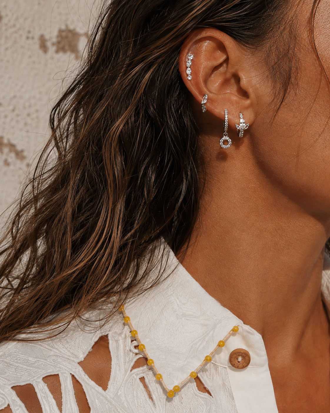 Silver ear stack by Galleria Armadoro featuring the Riviera Ear Climber and Lotus Huggie, styled in warm sunlight with a white embroidered shirt.