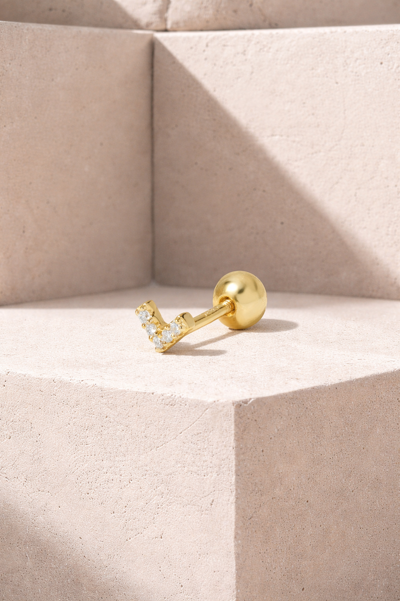 Tiny V-shaped gold vermeil stud earring with white CZ stones and ball screw back on neutral stone background