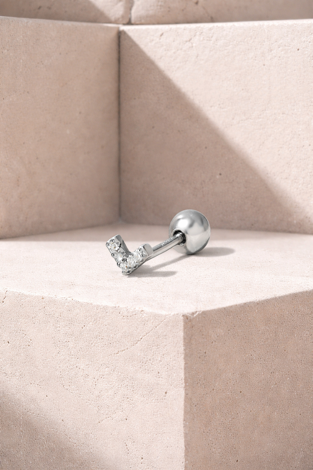Tiny V-shaped sterling silver stud earring with white CZ stones and ball screw back on neutral background
