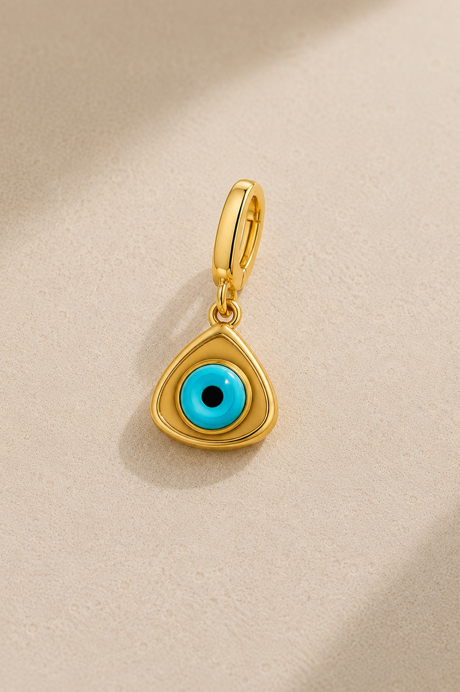 Gold triangle evil eye hook charm with turquoise eye bead on beige studio background