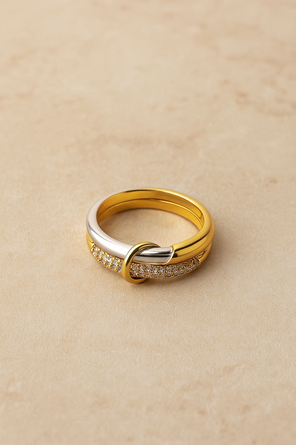 Nora Speira mixed-metal pavé ring on warm beige background, linked bands seen from above.
