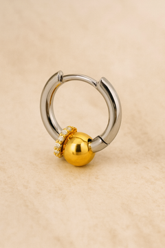 Two-tone Kora piercing bead huggie earring in sterling silver with gold bead and CZ halo on beige marble background