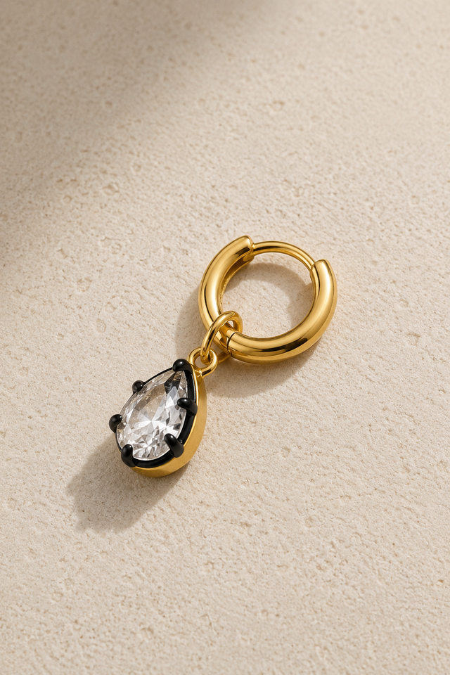 Gold 6.5mm huggie earring with Vittoria black and gold teardrop crystal charm on neutral stone background