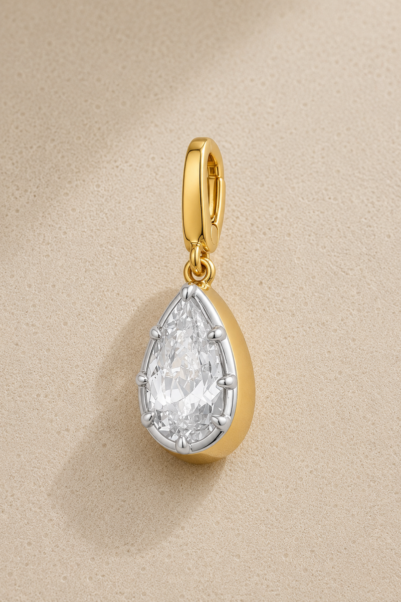 Vittoria teardrop crystal hook charm with gold plating and white rhodium details on beige studio background