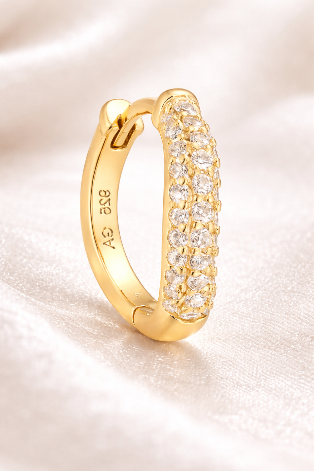 Close-up of Aurora Kyma gold pavé huggie earring on soft fabric background