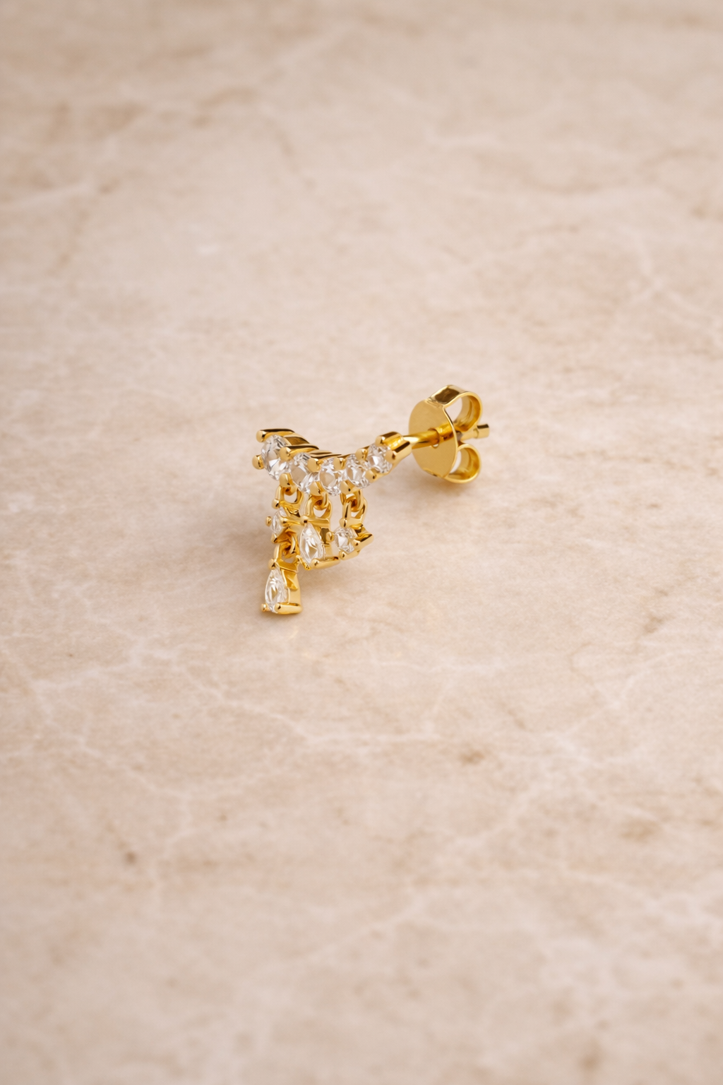 Drippy croissant gold vermeil stud earring with cascading crystal drops photographed on beige marble background