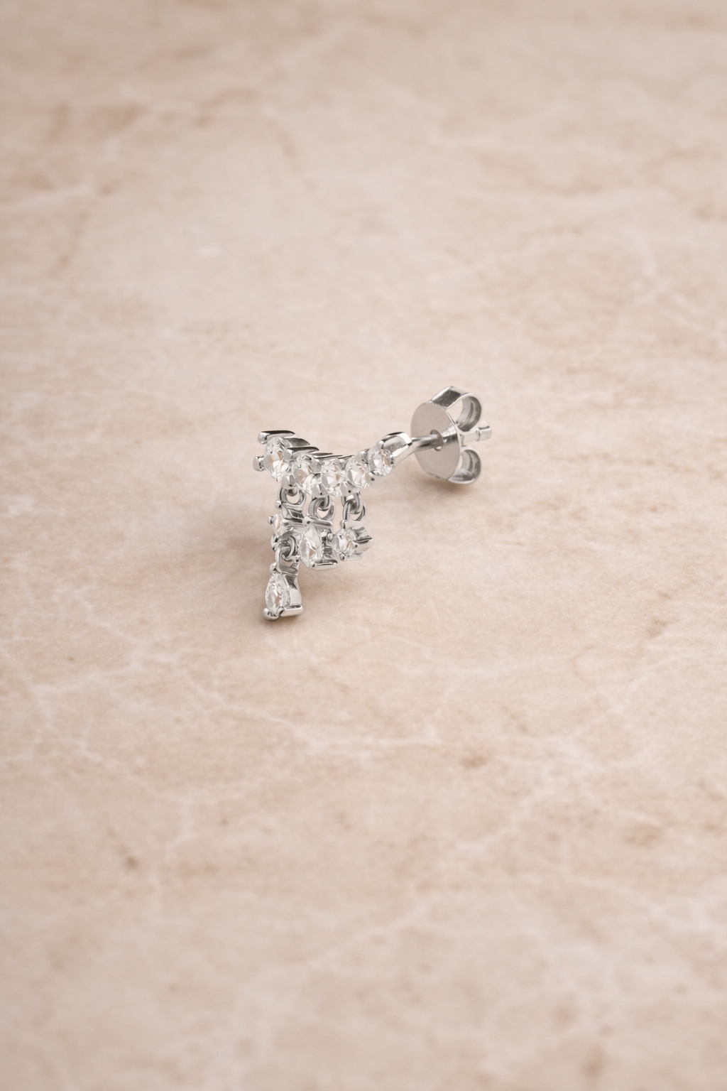 Drippy croissant sterling silver stud earring with cascading crystal drops photographed on beige marble background