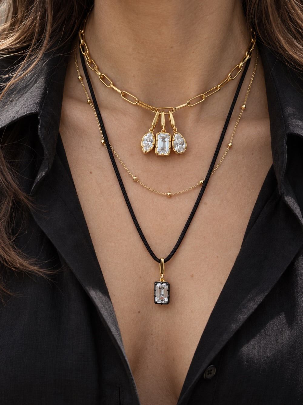 Layered Galleria Armadoro necklaces featuring three Vittoria charms on a gold chain, the Charlotte Beaded Station Chain and a black cord with an emerald-cut Vittoria charm.