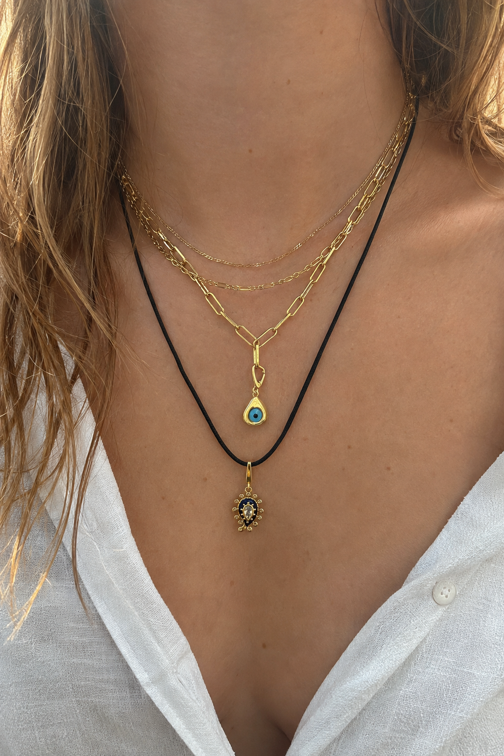 Layered gold necklaces by Galleria Armadoro with fine gold chains, a paperclip chain, black cord and two evil eye charms.