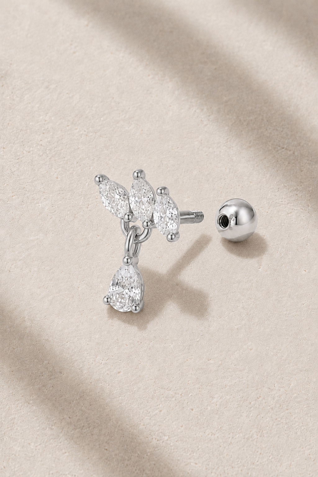 Silver floral ball screw piercing stud with white CZ stones on neutral stone background