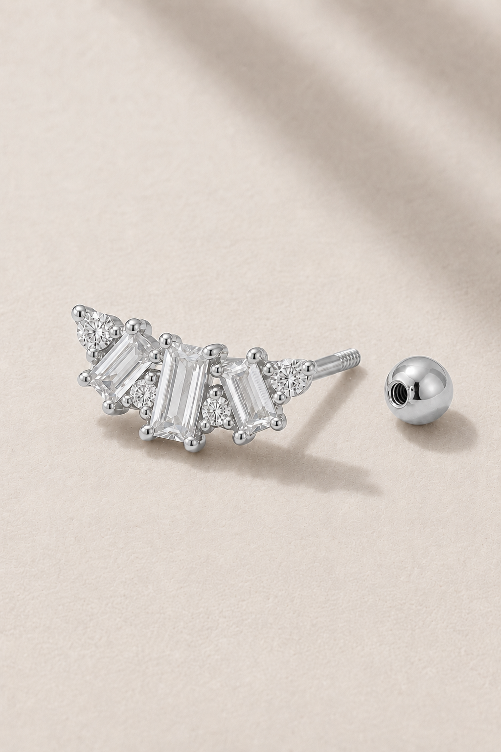 Silver Art Deco ball screw piercing stud with white CZ stones on neutral stone background