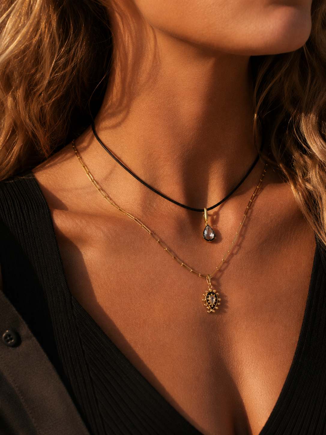 Layered gold necklaces styled by Galleria Armadoro with a black cord, teardrop pendant, fine gold chain and paisley charm.