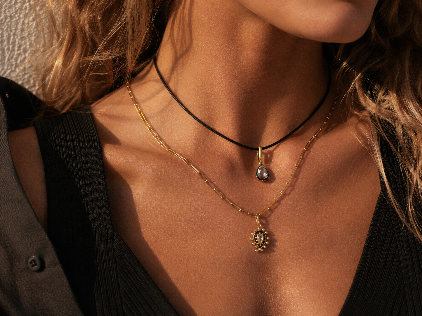 Layered gold necklaces styled by Galleria Armadoro with a black cord, teardrop pendant, fine gold chain and paisley charm.