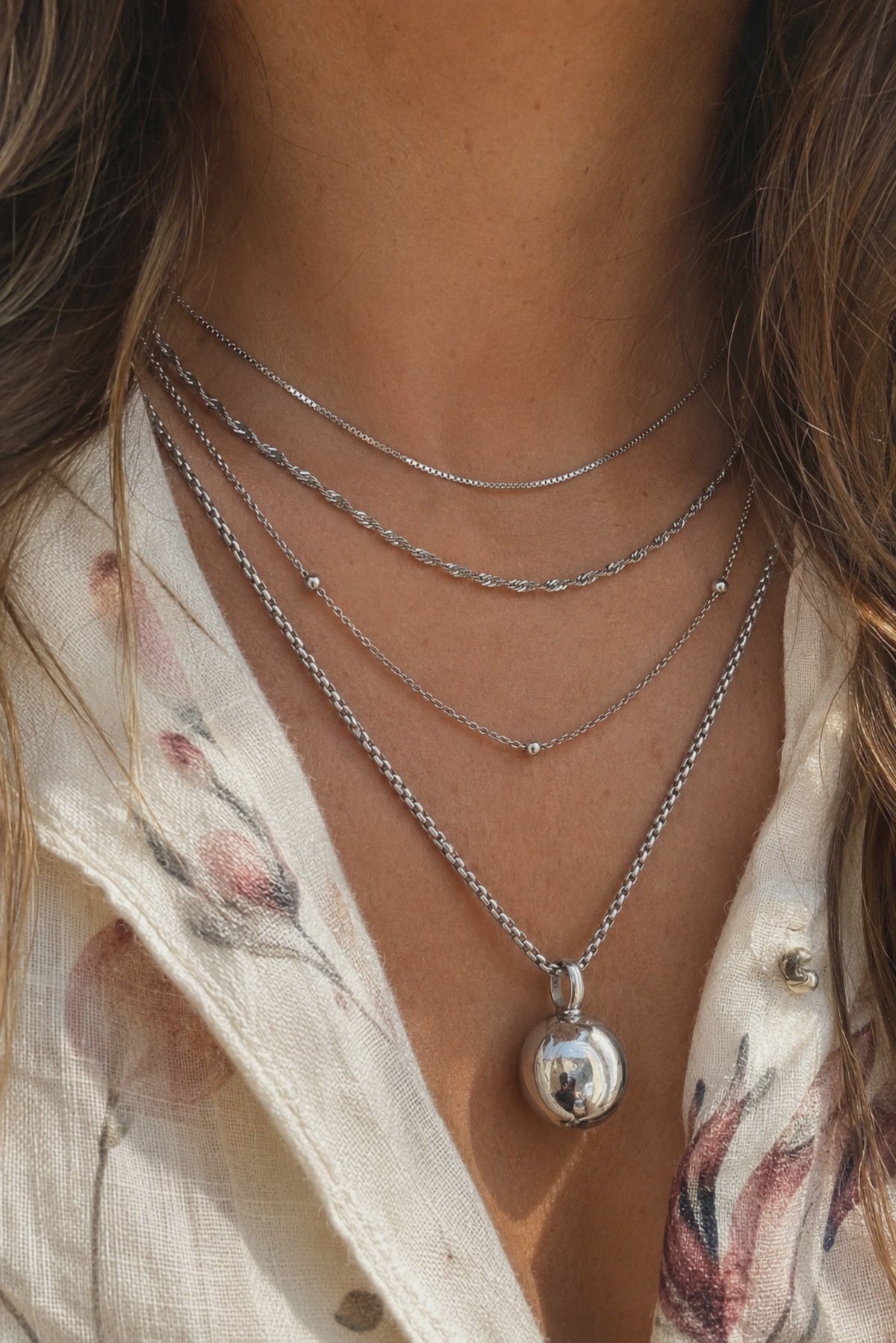 Layered silver necklaces by Galleria Armadoro styled with fine chains, textured silver chains and a sculptural silver pendant.