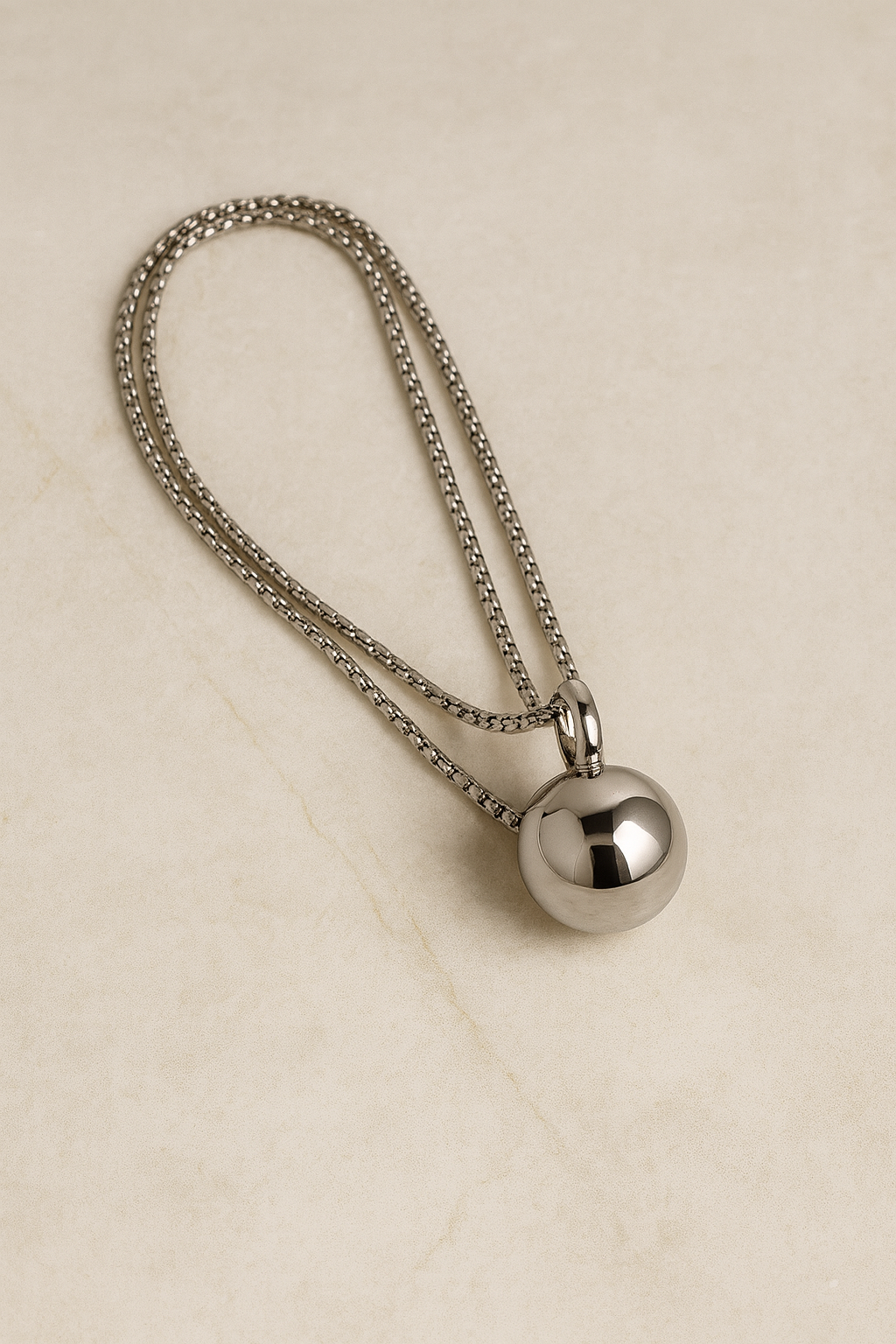 Flatlay of Riva silver sphere pendant necklace on marble background, adjustable chain