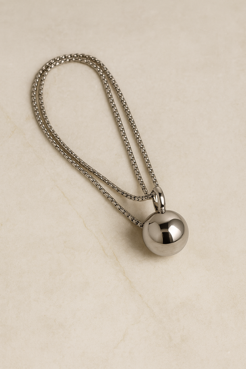 Flatlay of Riva silver sphere pendant necklace on marble background, adjustable chain